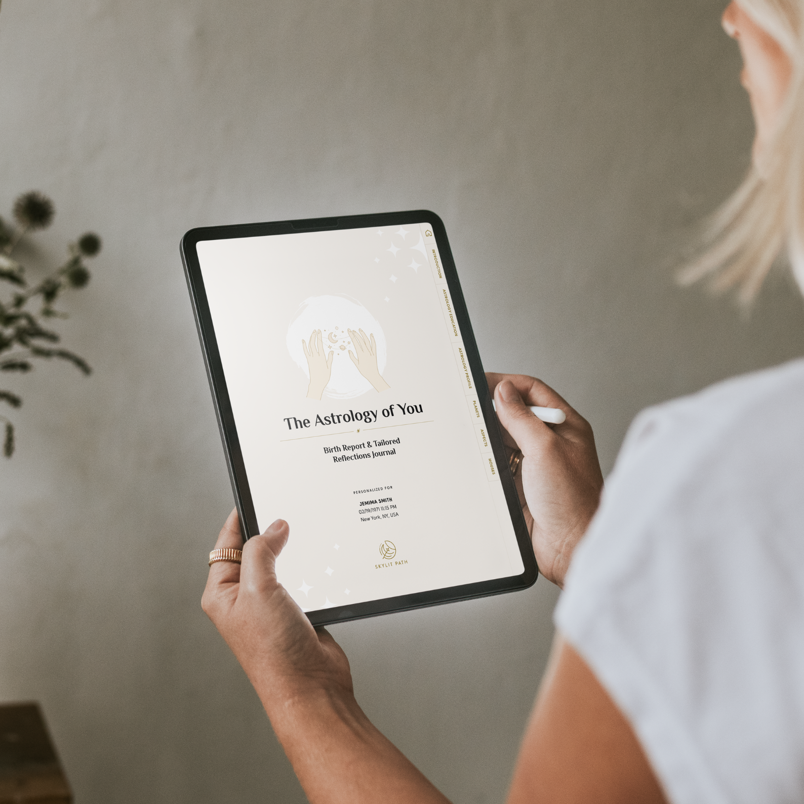 Woman holding a tablet with 'The Astrology of You' app displayed on a neutral background
